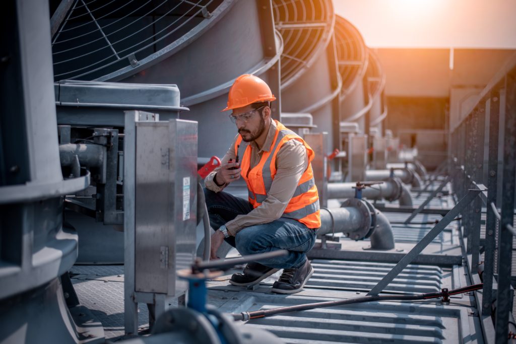 A man in an orange safety vest is inspecting an industrial air compressor.
